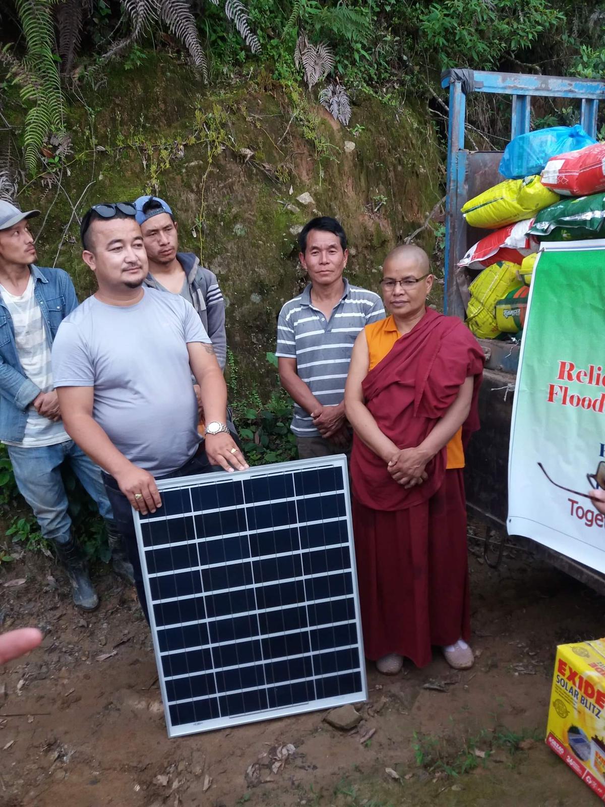 Local team and a monastic beside a solar panel and relief supplies