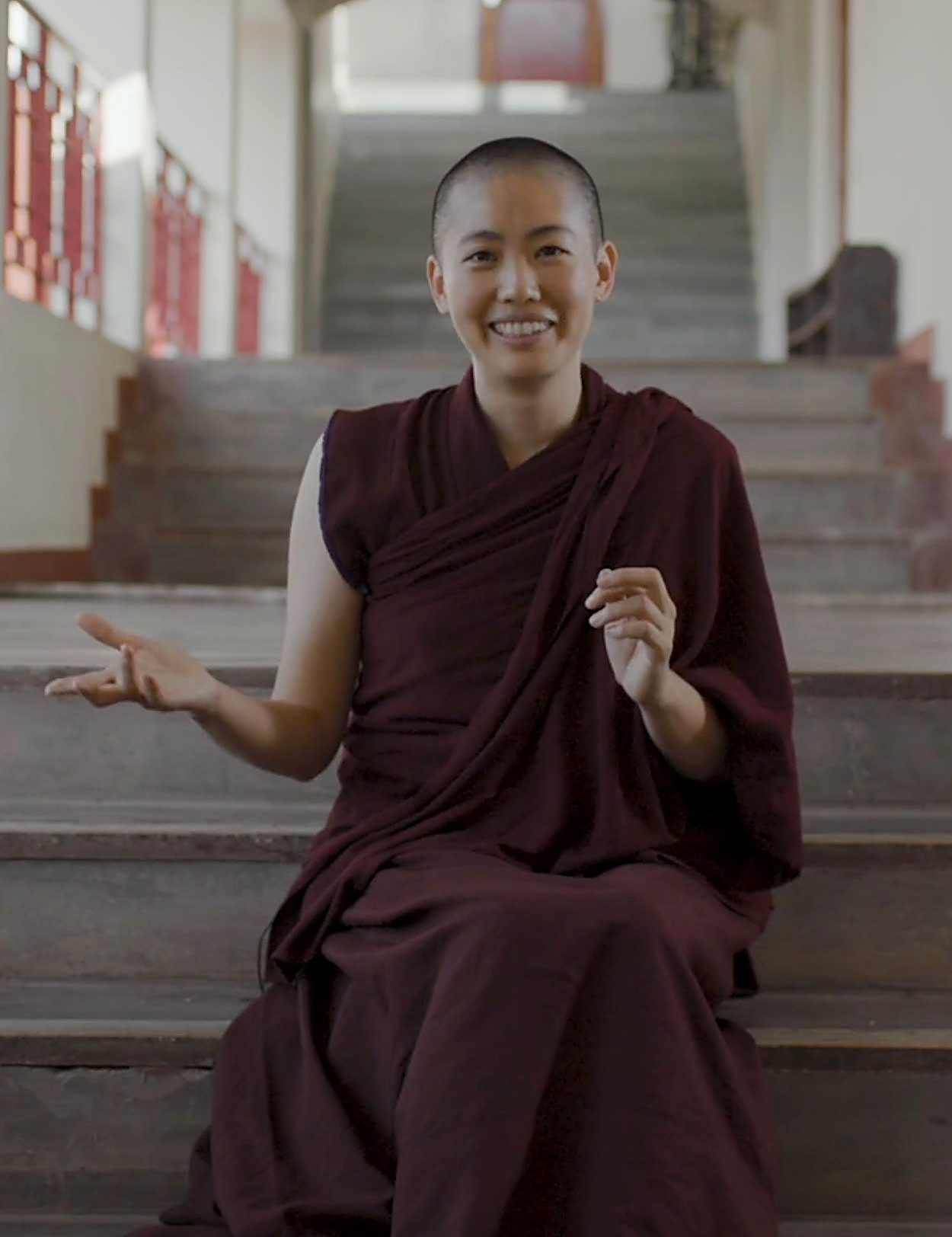 A young Geshe-ma in maroon robes smiling on the monastery steps