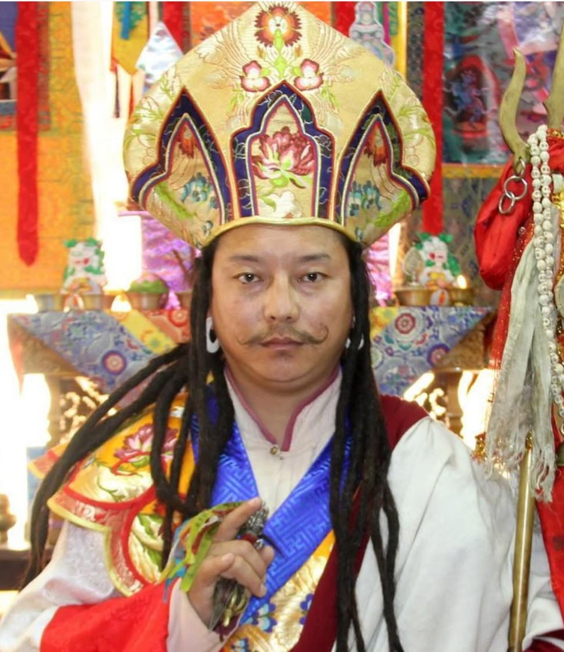 A Tibetan Buddhist lineage holder in elaborate ceremonial brocade hat and robes, supported by The Maitri Project