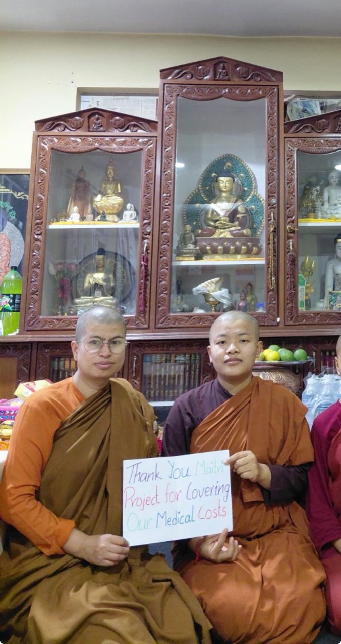 Two monastics holding a thank-you sign for Maitri medical-cost support