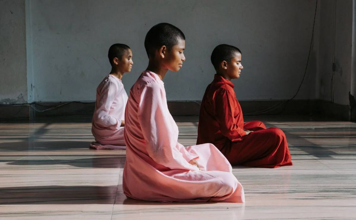 Young nuns in pink and red robes seated in meditation, The Maitri Project