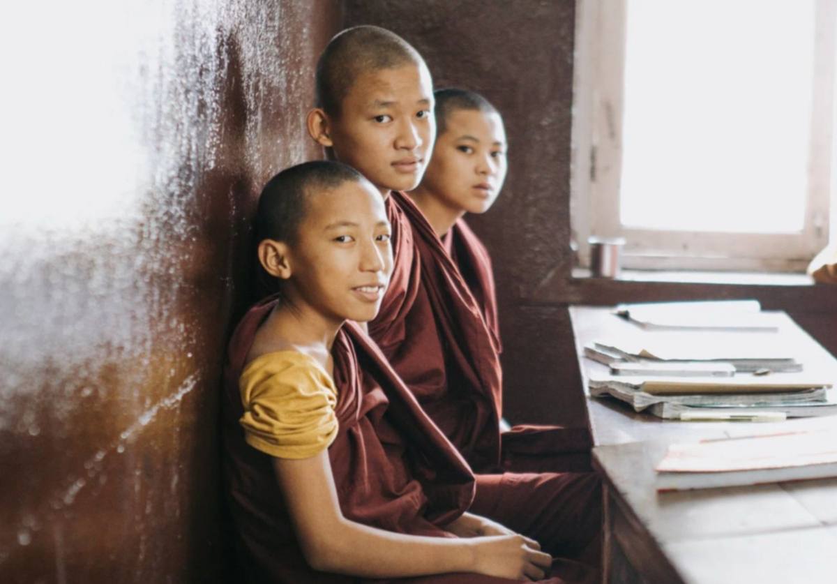 A nun teaching young monastic students gathered around an open notebook