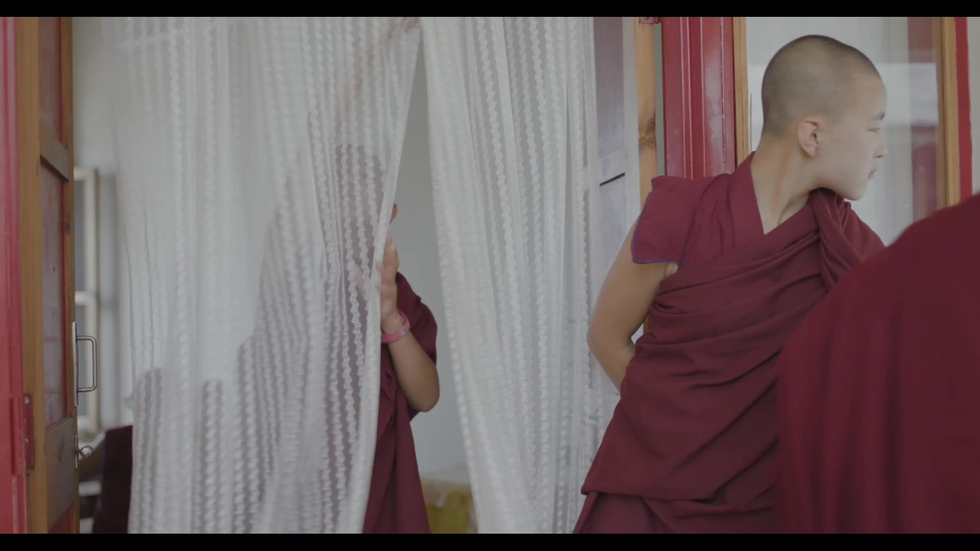 A nun standing in a curtained doorway — still from Rise of the Geshe-Ma